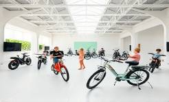 airy ebike dealership, spacious, children playing with ebike models, photorealistic, large open space with high ceilings and skylights, highly detailed, playful and family-friendly, bright whites and baby blues, diffused natural lighting, shot with a high-angle lens.